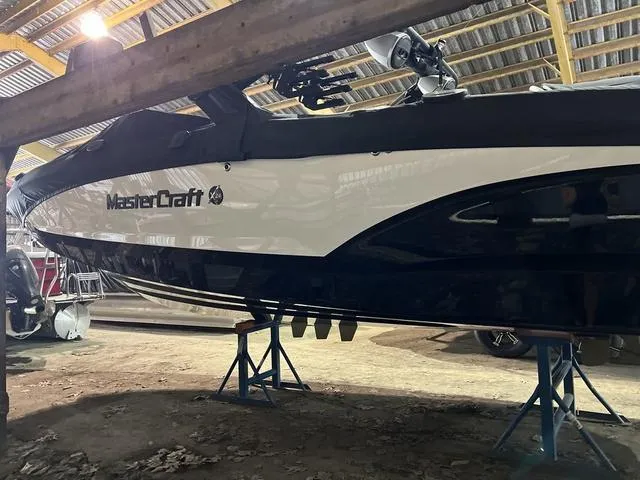 Slide: The Image of 2024 MasterCraft X24 boat in storage, elevated on stands, under a wooden roof. - 3