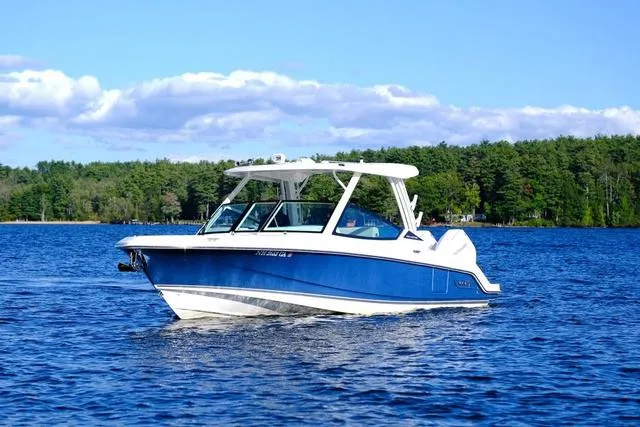 Slide: The Image of 2024 Boston Whaler 280 Vantage boat cruising on a serene lake with forested shoreline. - 11