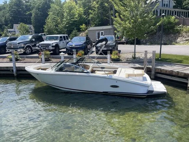 Slide: The Image of 2022 Cobalt CS23 boat docked in clear water, surrounded by parked cars and lush greenery. - 2