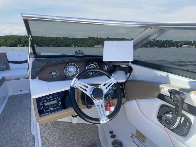 Slide: The Image of 2015 Four Winns H230 boat dashboard with steering wheel and controls on a lake. - 9