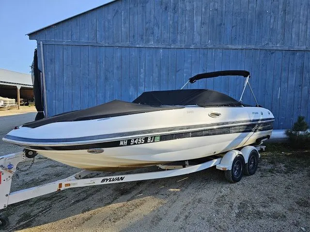 Slide: The Image of 2004 Sylvan 2080 I/O boat on trailer, parked by a blue wooden building. - 1