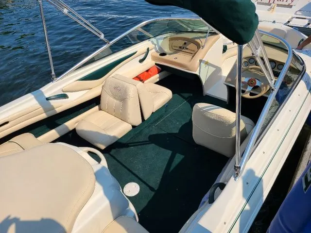 Slide: The Image of 2000 Sea Ray 185BR boat interior with beige seating and green carpet, docked on water. - 4