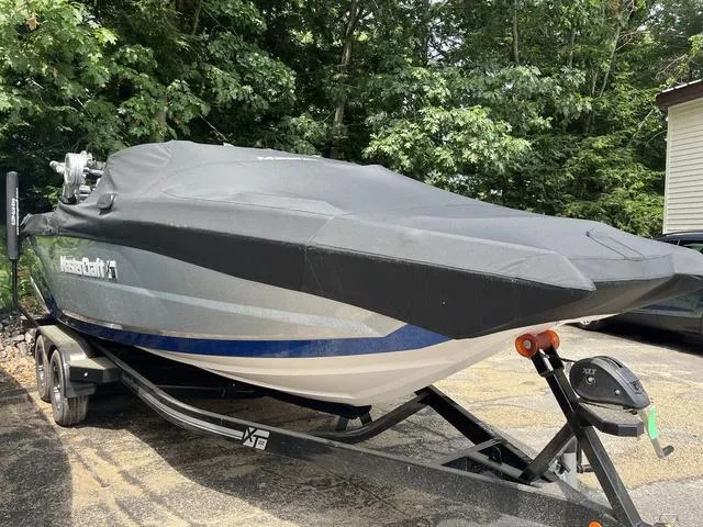 Slide: The Image of 2021 MasterCraft XT22 boat covered on trailer, parked outdoors near trees. - 5