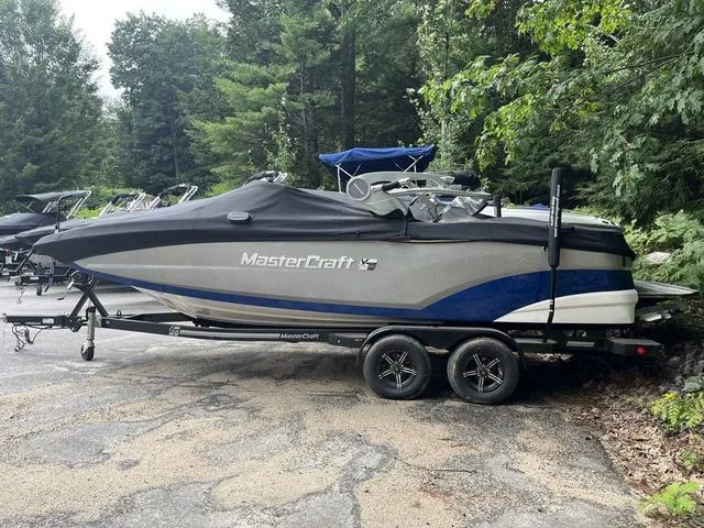 Slide: The Image of 2021 MasterCraft XT22 boat on trailer, covered, parked in wooded area. - 6