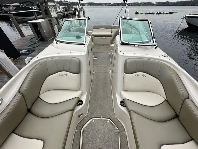 Slide: The Image of 2005 Sea Ray 240 Sundeck boat interior with beige seating, docked by the water. - 12