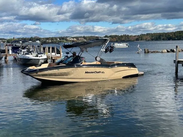 Slide: The Image of 2023 MasterCraft NXT22 boat on a lake with a scenic background. - 2