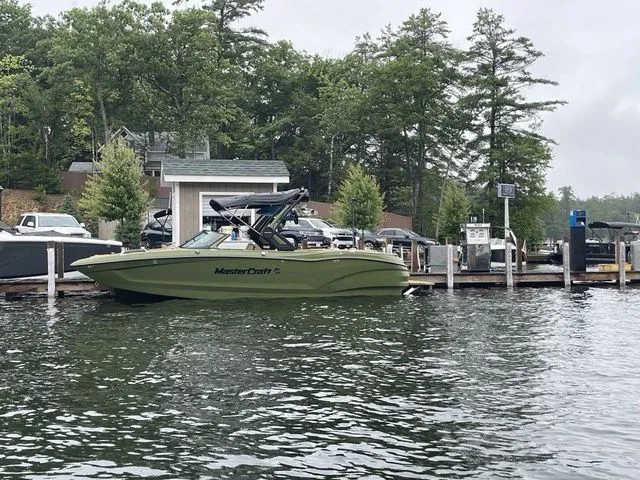 Slide: The Image of 2023 MasterCraft X24 boat docked on a serene lake with lush trees in the background. - 1