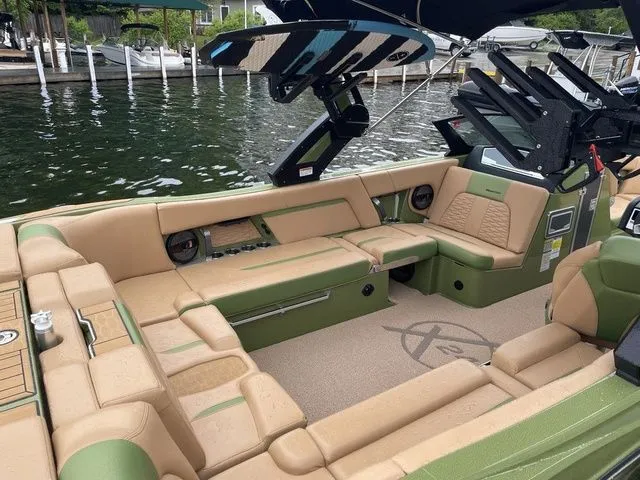Slide: The Image of 2023 MasterCraft X24 boat interior with tan and green seating, docked by a lake. - 11