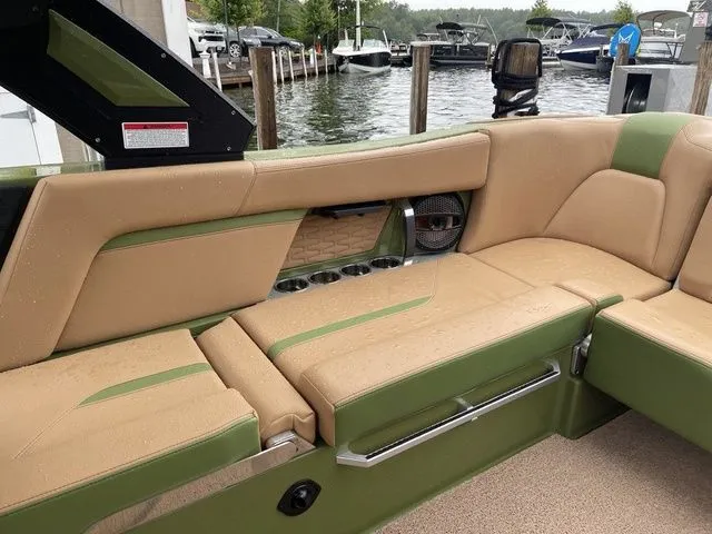 Slide: The Image of 2023 MasterCraft X24 boat interior with tan and green seating, docked by a lake. - 6