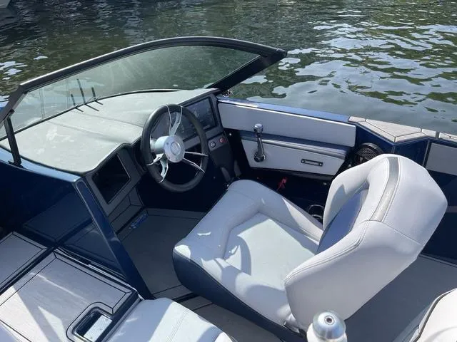 Slide: The Image of 2024 MasterCraft ProStar boat interior with steering wheel and seating, on calm water. - 6