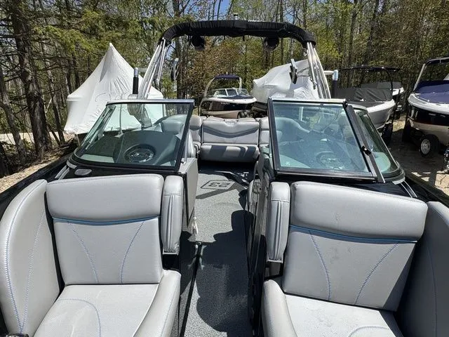 Slide: The Image of 2018 MasterCraft X23 boat interior with gray seating and open windshield, surrounded by trees. - 19