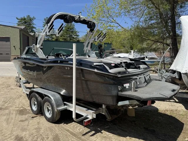 Slide: The Image of 2018 MasterCraft X23 boat on trailer, parked outdoors, surrounded by trees and buildings. - 3