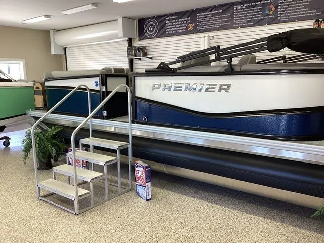 Slide: The Image of 2025 Premier 200 SUNSCAPE RE-CL pontoon boat displayed indoors with metal stairs. - 2