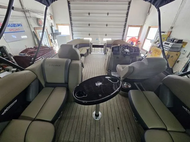 Slide: The Image of 2025 Sylvan Mirage X1 pontoon boat interior with seating and table in a garage setting. - 14