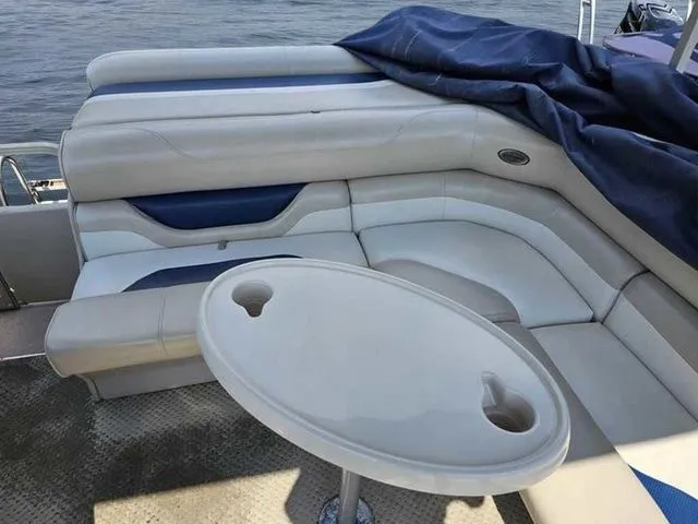 Slide: The Image of 2006 Sylvan Mirage 8520 boat interior with cushioned seating and table on a calm lake. - 11
