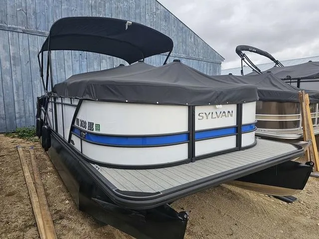 Slide: The Image of 2022 Sylvan L-3 CLZ pontoon boat with cover, parked outdoors near a blue building. - 3