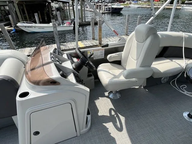Slide: The Image of 2022 Sylvan 8520 LZ boat interior with steering console and seating at a marina. - 11