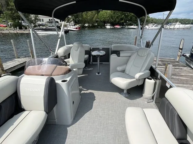 Slide: The Image of 2022 Sylvan 8520 LZ pontoon boat interior with seating, table, and canopy on a lake. - 7