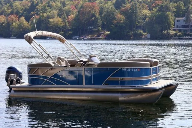 Slide: The Image of 2022 Sylvan 8520 LZ pontoon boat on a serene lake with forested background. - 1