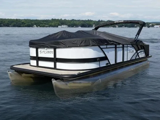 Slide: The Image of 2022 Sylvan L-3 CLZ pontoon boat on a calm lake with a black cover. - 1