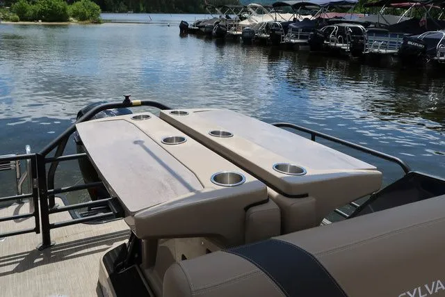 Slide: The Image of 2023 Sylvan L-3 DLZ BAR pontoon boat with seating and cup holders on a calm lake. - 16