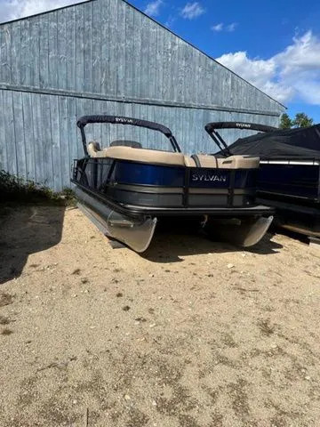 Slide: The Image of 2023 Sylvan L-3 DLZ BAR pontoon boat parked on gravel near a blue building. - 21