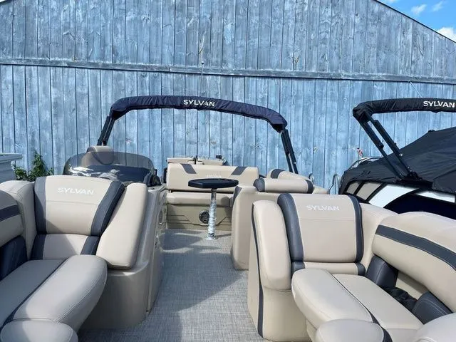 Slide: The Image of 2023 Sylvan L-3 DLZ BAR pontoon boat with beige seating and canopy, docked by a blue wall. - 22