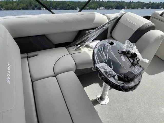 Slide: The Image of 2023 Sylvan X3 CLZ boat interior with gray seating and a small table, near a lake. - 4