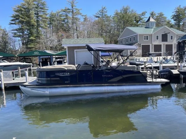 Slide: The Image of 2023 Sylvan L-5 CLZ pontoon boat docked at a marina with trees and buildings in the background. - 3