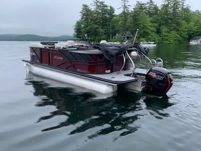 Slide: The Image of 2023 Sylvan X1 pontoon boat on a serene lake with lush green trees. - 4
