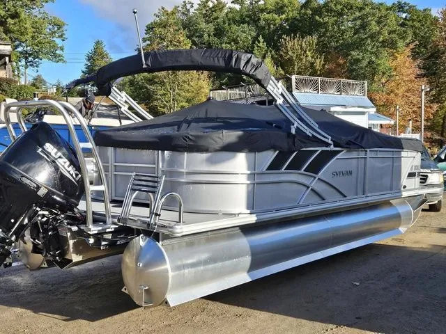 Slide: The Image of 2023 Sylvan 8524 Mirage LZ pontoon boat with Suzuki outboard motor, covered and parked outdoors. - 3