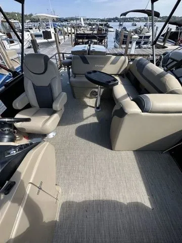 Slide: The Image of 2023 Sylvan L-5 DLZ Bar pontoon boat interior with plush seating and table, docked at marina. - 7