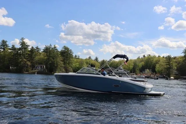 Slide: The Image of 2023 Cobalt CS22 boat cruising on a scenic lake with trees and blue sky. - 13