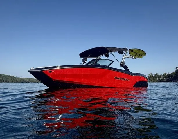 Slide: The Image of 2024 MasterCraft NXT23 boat on a calm lake under clear blue sky. - 1