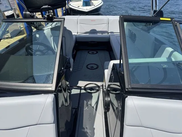 Slide: The Image of 2024 MasterCraft NXT23 boat interior with gray seating and open windshield, docked by the water. - 19