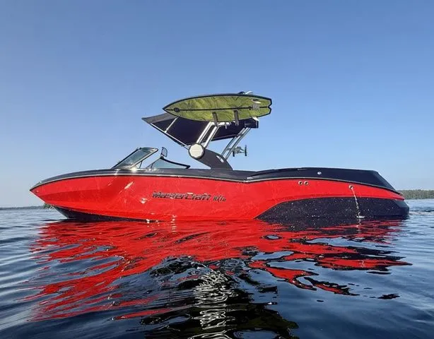 Slide: The Image of 2024 MasterCraft NXT23 boat in vibrant red on calm water, with a wakeboard rack. - 5