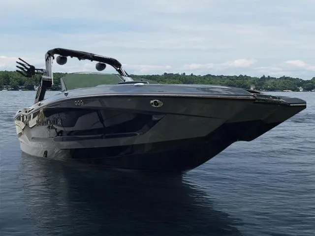 Slide: The Image of 2024 MasterCraft X24 boat on calm lake with lush green shoreline. - 1