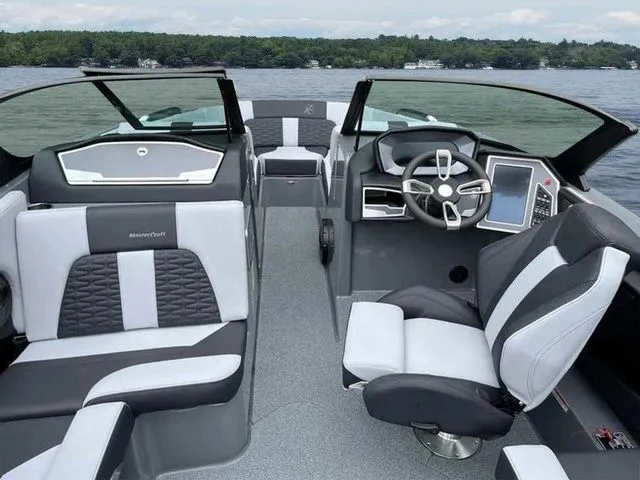 Slide: The Image of 2024 MasterCraft X24 boat interior with modern seating and steering, on a calm lake. - 15