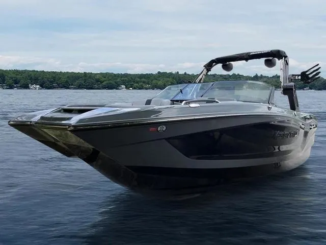 Slide: The Image of 2024 MasterCraft X24 boat on a lake, sleek design, calm water, and forested shoreline. - 2