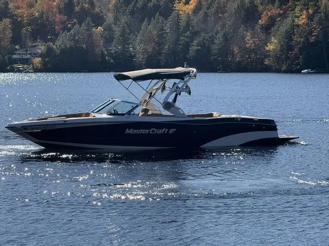 Slide: The Image of 2019 MasterCraft XT25 boat on a serene lake with autumn foliage in the background. - 1