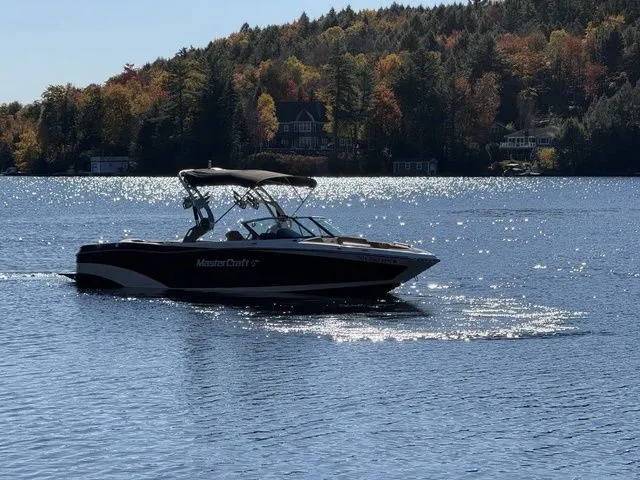 Slide: The Image of 2019 MasterCraft XT25 boat cruising on a scenic lake with autumn foliage. - 2