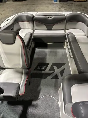 Slide: The Image of 2019 MasterCraft XT22 boat interior with gray and white seating, red accents, and logo on carpet. - 6