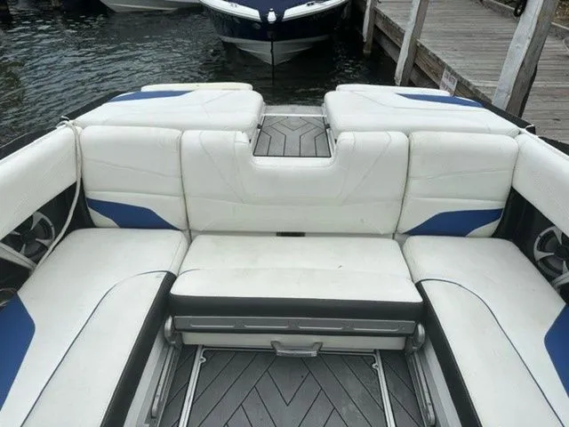 Slide: The Image of 2017 Malibu 24 MXZ boat interior with white and blue seating, docked by wooden pier. - 12