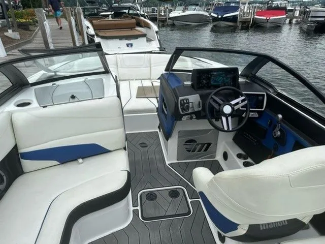 Slide: The Image of 2017 Malibu 24 MXZ boat interior with white and blue seating, docked at a marina. - 14