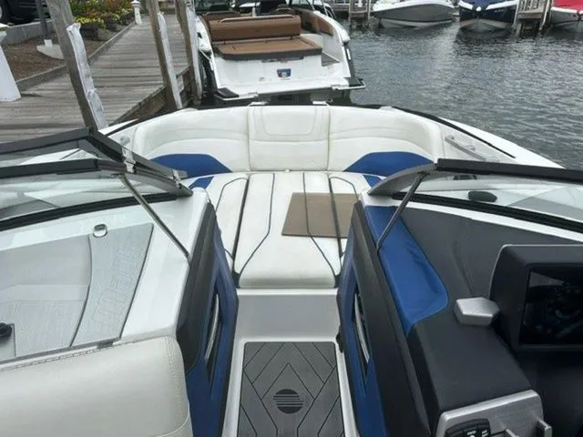 Slide: The Image of 2017 Malibu 24 MXZ boat interior with white and blue seating, docked by the water. - 17