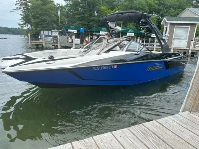 Slide: The Image of 2017 Malibu 24 MXZ boat docked on a lake with lush greenery in the background. - 19
