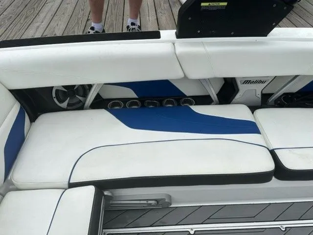Slide: The Image of 2017 Malibu 24 MXZ boat interior with white and blue seating, cup holders, and deck view. - 4