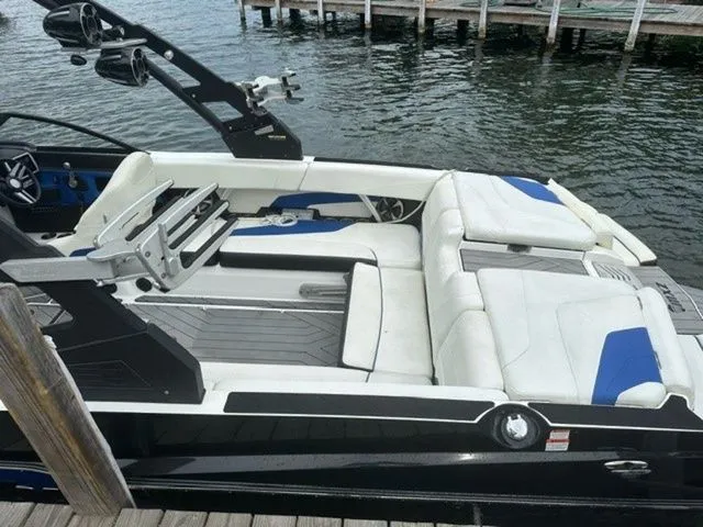 Slide: The Image of 2017 Malibu 24 MXZ boat with white and blue seating, docked by the water. - 5