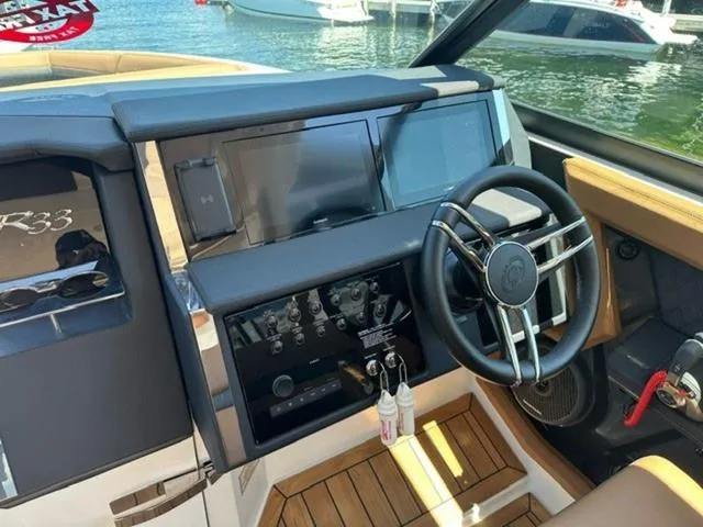Slide: The Image of 2024 Cobalt R33 Surf boat dashboard with steering wheel and control panel, docked by the water. - 11