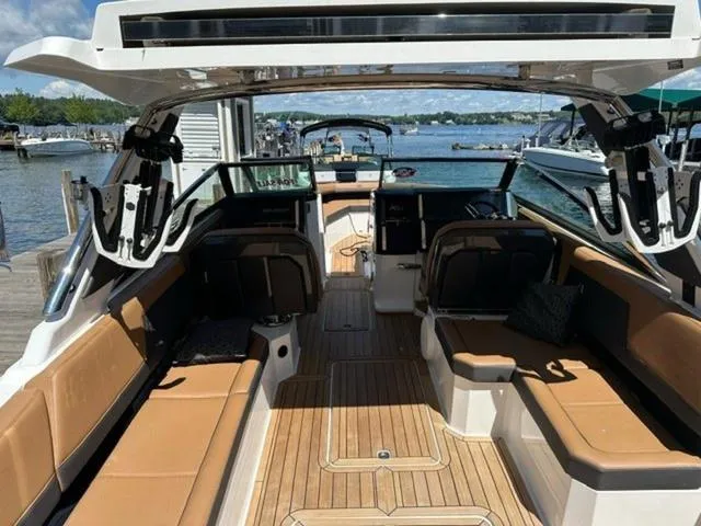 Slide: The Image of 2024 Cobalt R33 Surf boat interior with tan seating and wood flooring at a marina. - 2